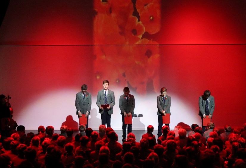 Boys stand with bowed heads in front of a backdrop of poppies as they read names of Heath Mount pupils who lost their lives in the world wars